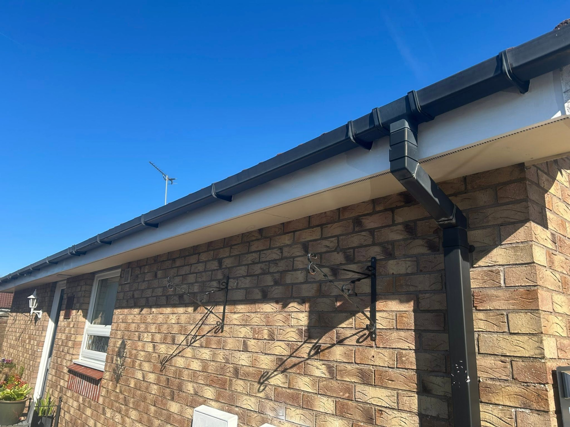 Neatly finished black guttering, downpipes and white fascia on a brick home